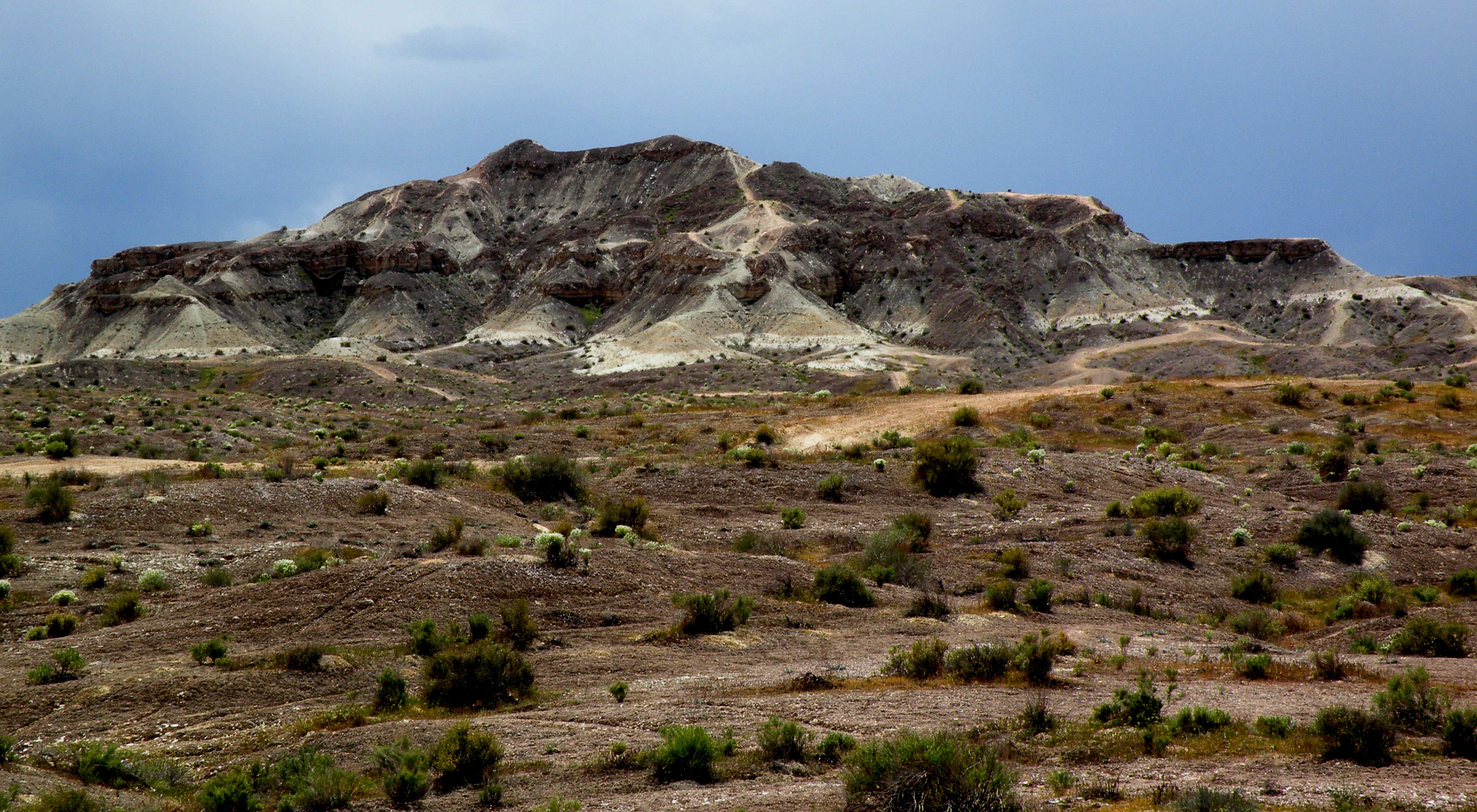 Landscape view of brown scrubby hills leading up to a large brown rock formation in the distance.