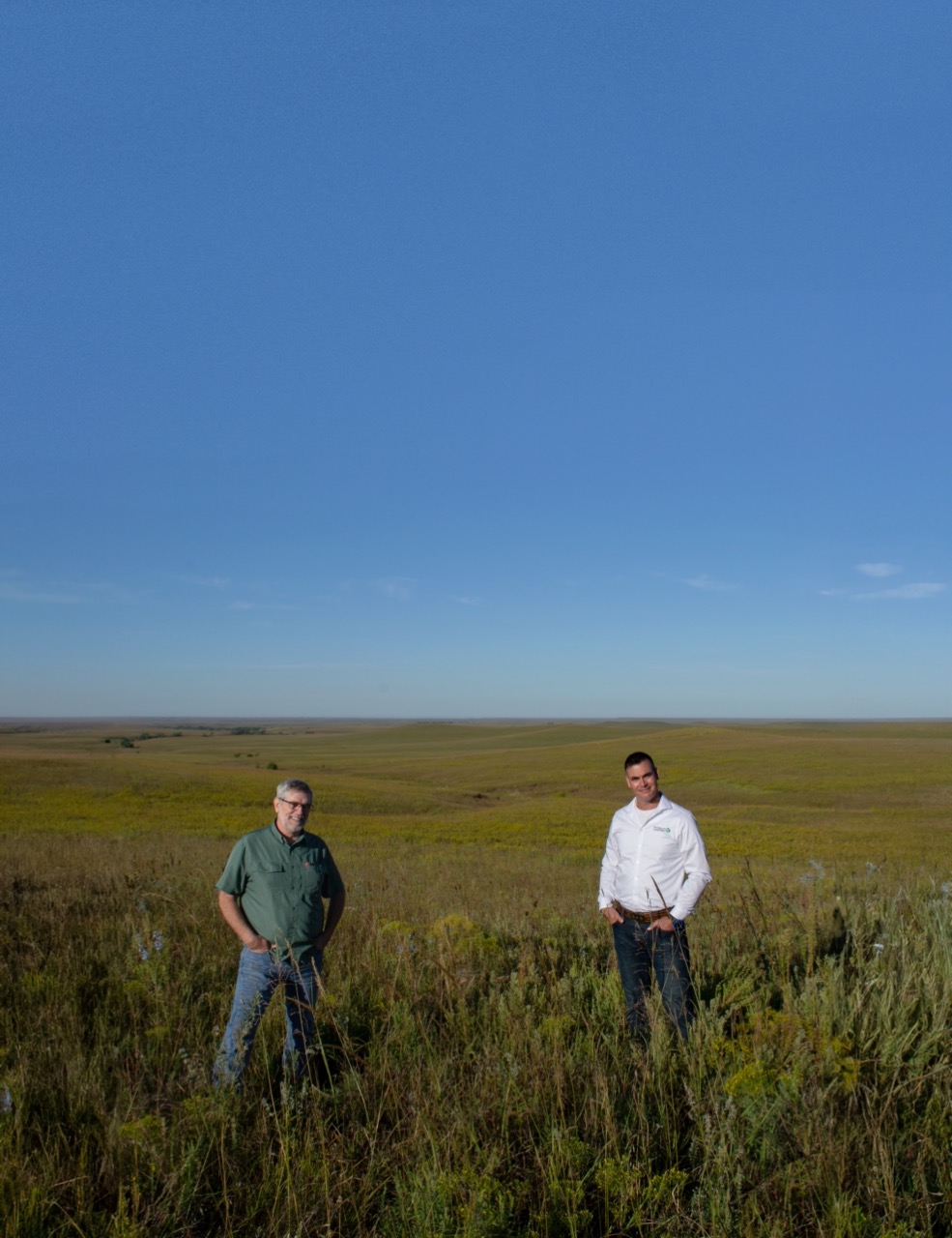 Two smiling men in a green field of grass.