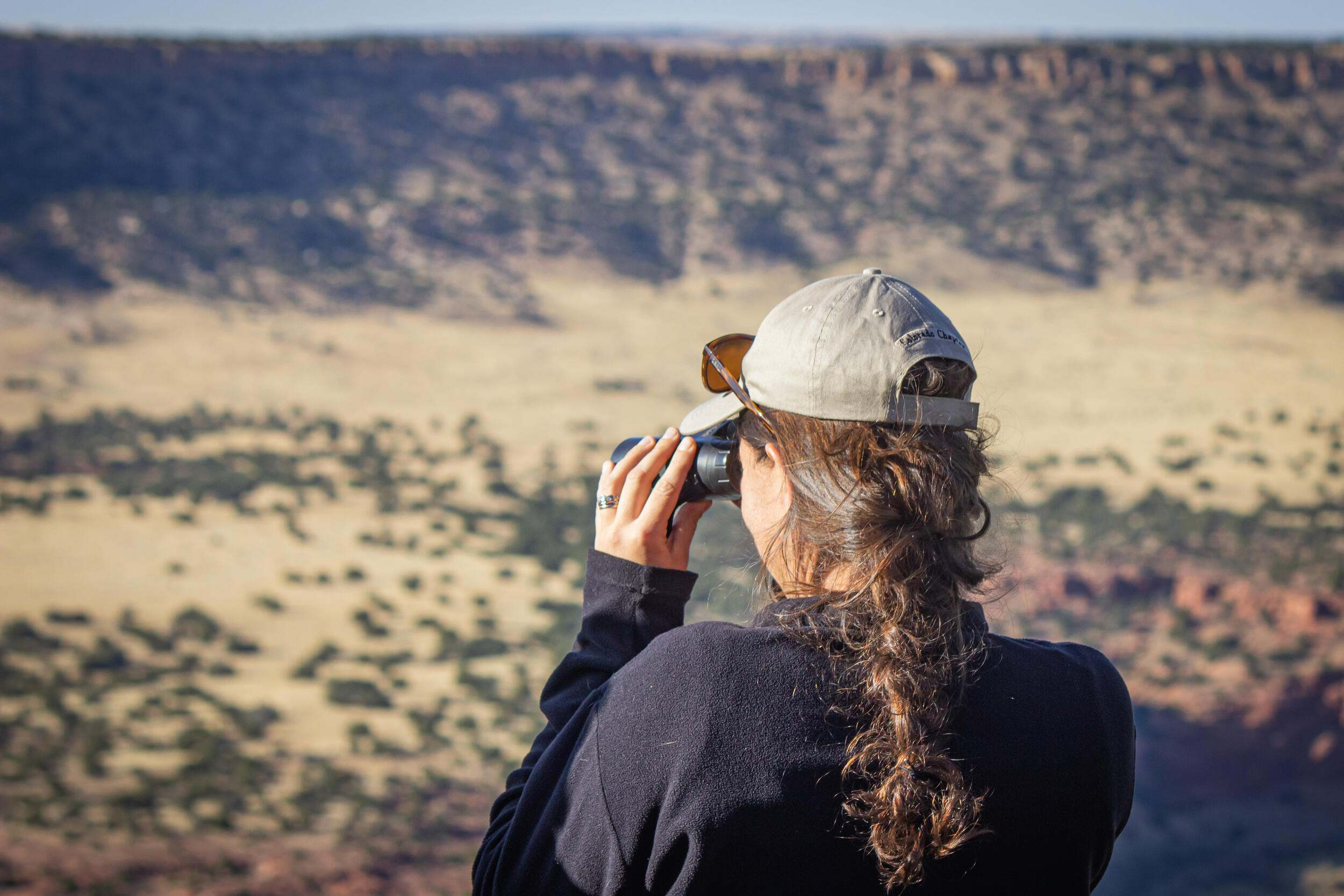 A woman looking through binoculars into a canyon.