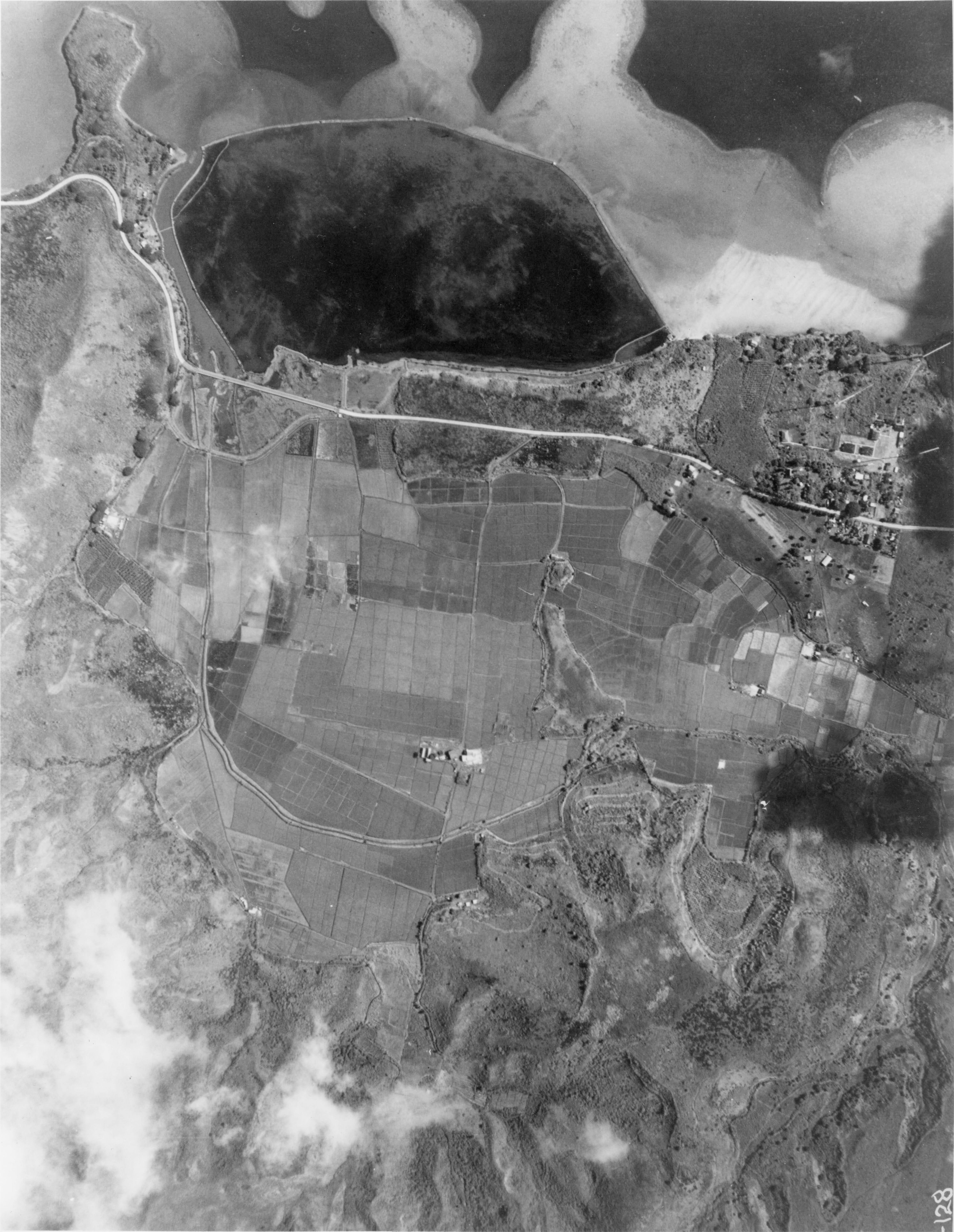 Aerial black-and-white photo from 1928 with He‘eia nearshore reefs and fishpond at the top, wetlands covered in taro fields in the center, and edges of lowlands below.