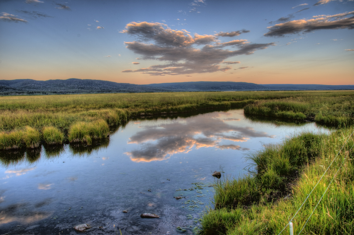 A river meanders through a grassy landscape at sunset.