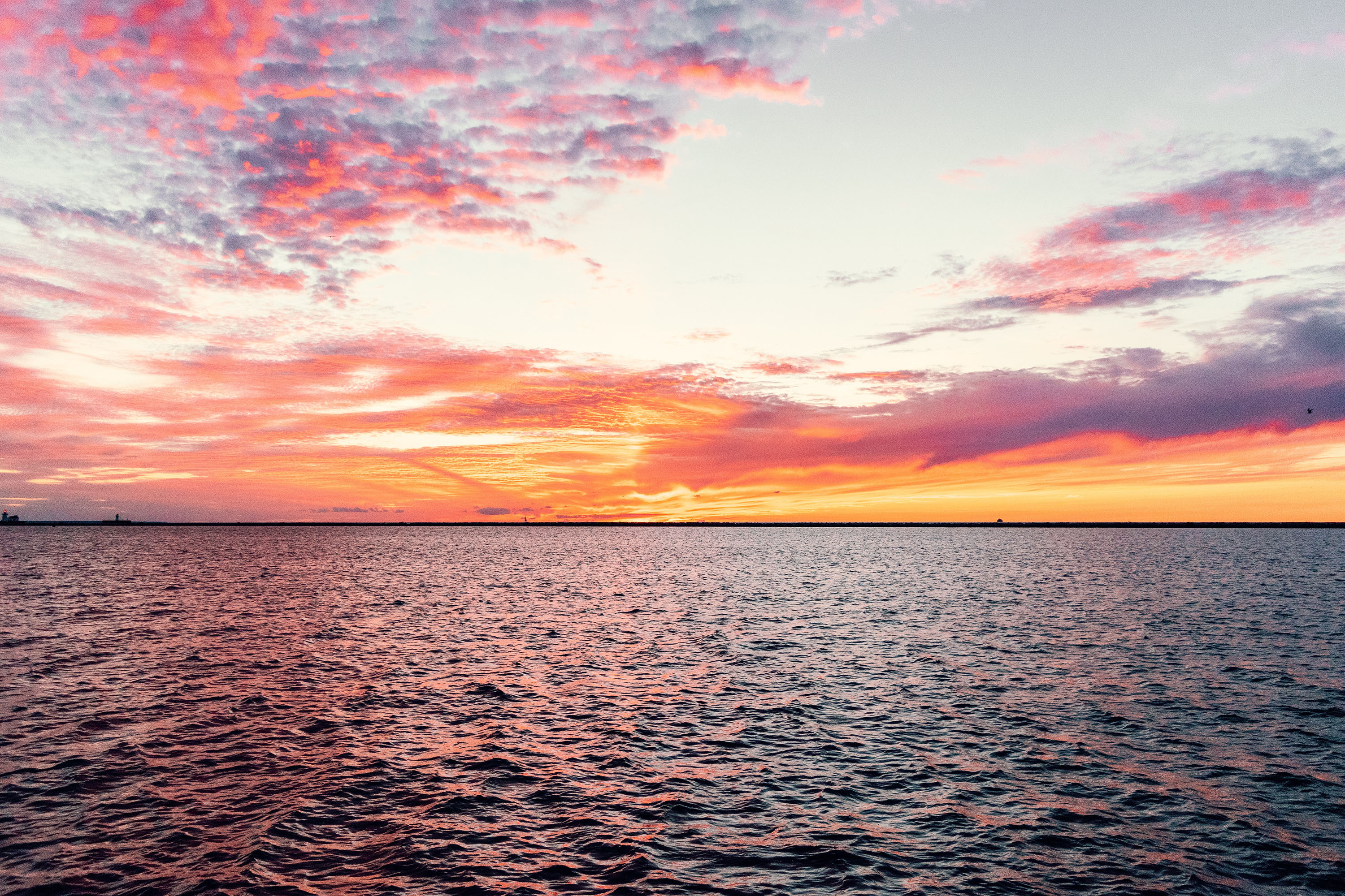 A sunset in a pink-orange sky over the waters of Lake Erie. 