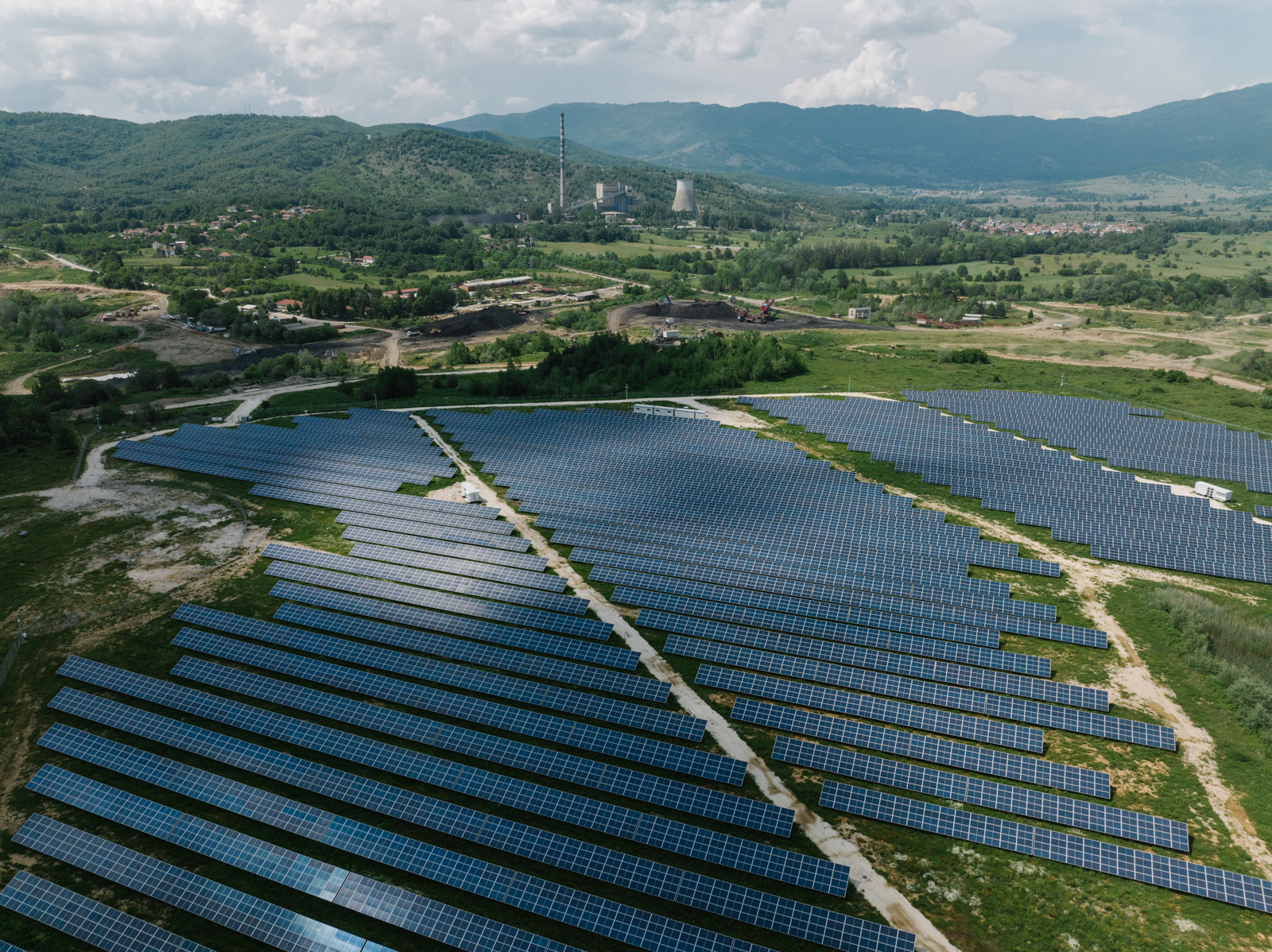 Aerial view of a field of solar panels in a wide, green landscape.