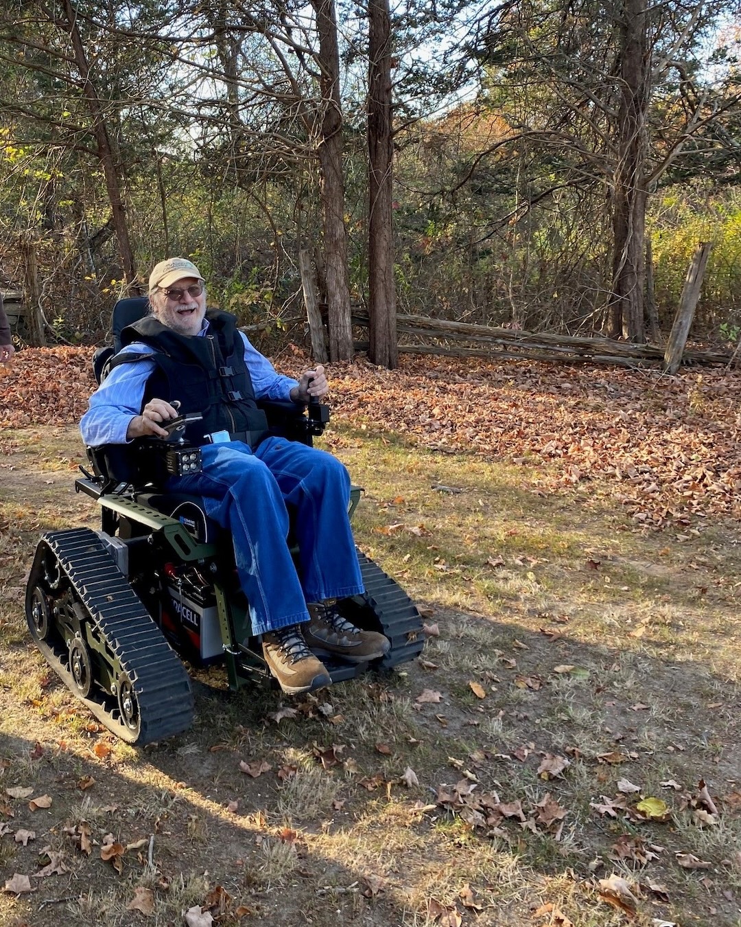 A man wearing a hat and sunglasses sits in a wheelchair with big tires.