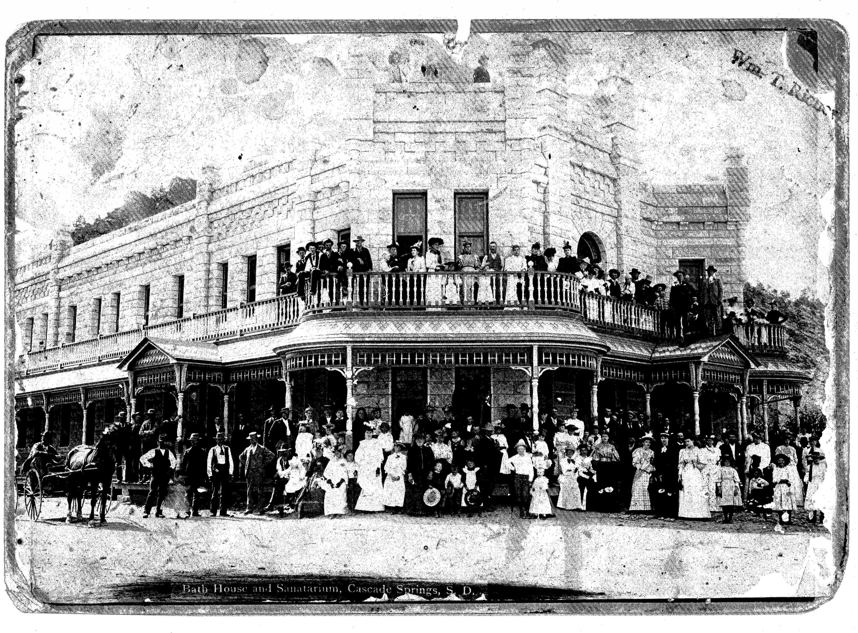 A historic photo of many people standing around a stone building.