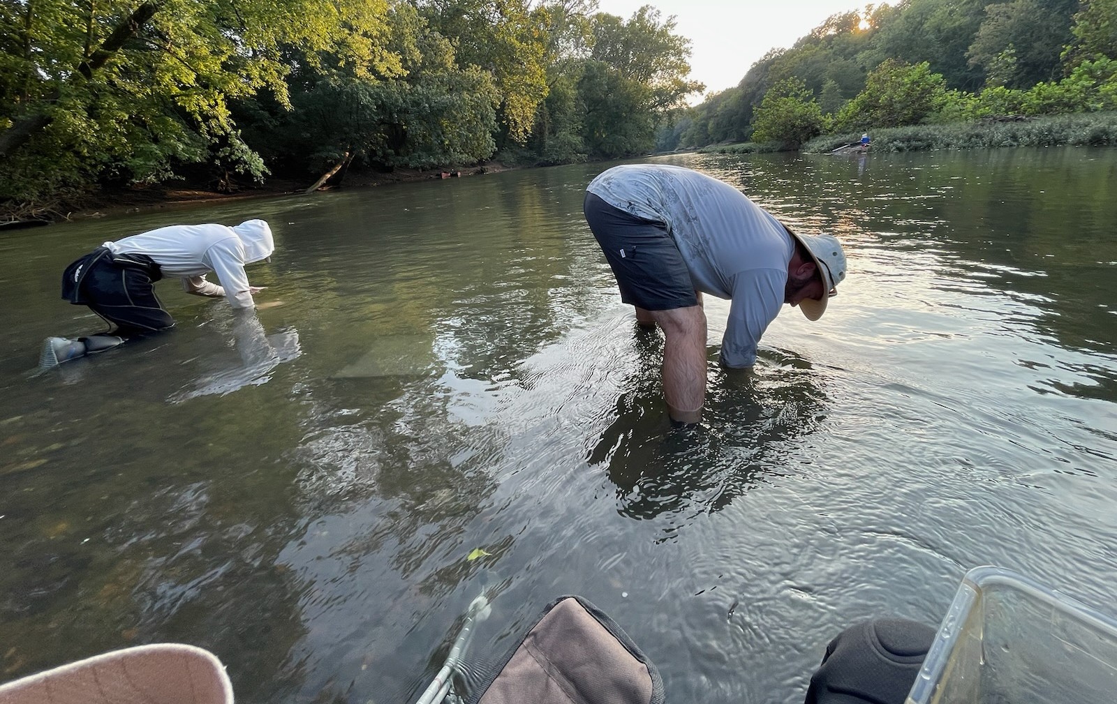 Two people bend over to examine a creek.