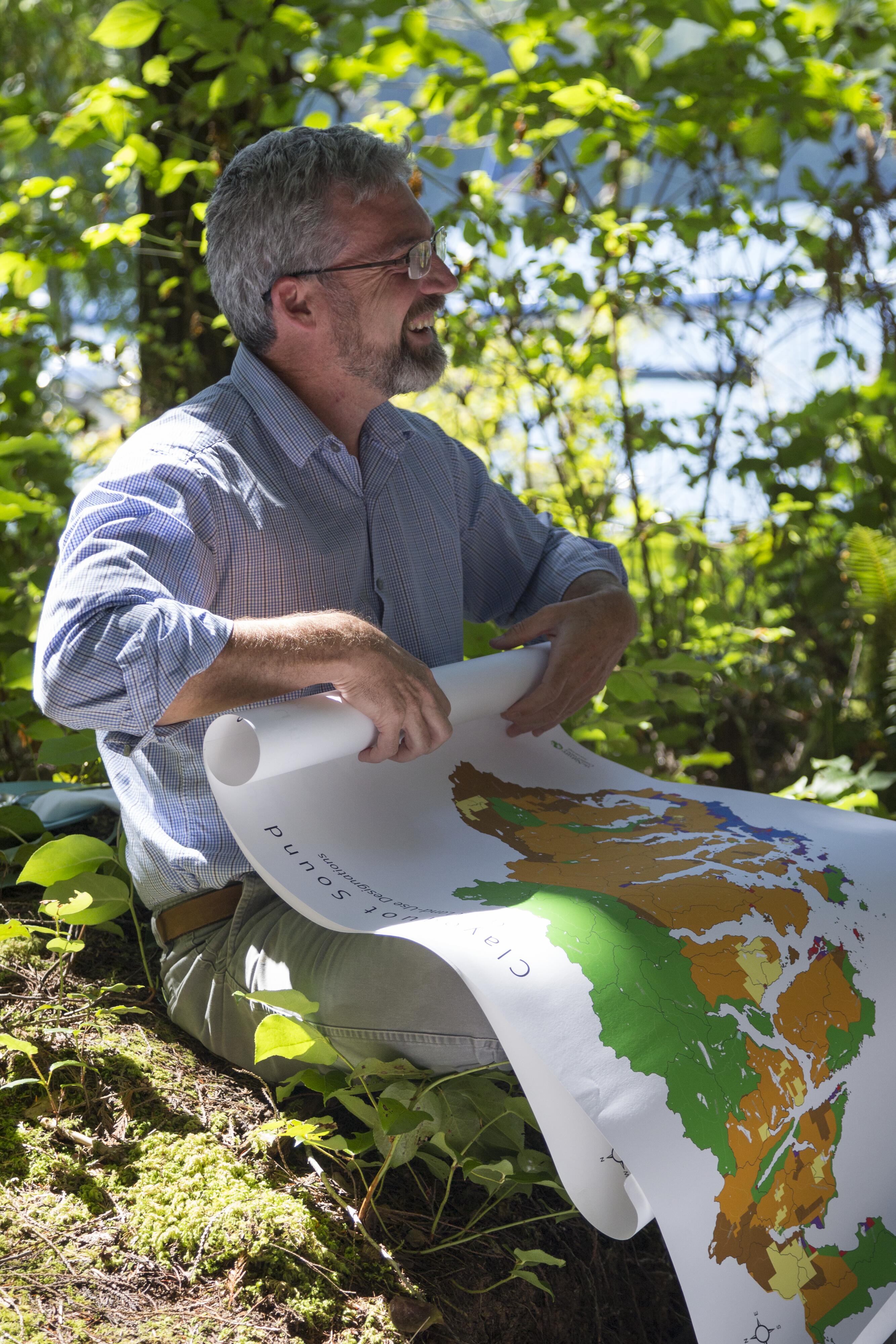 A person sitting in a natural setting rolling up a large map.