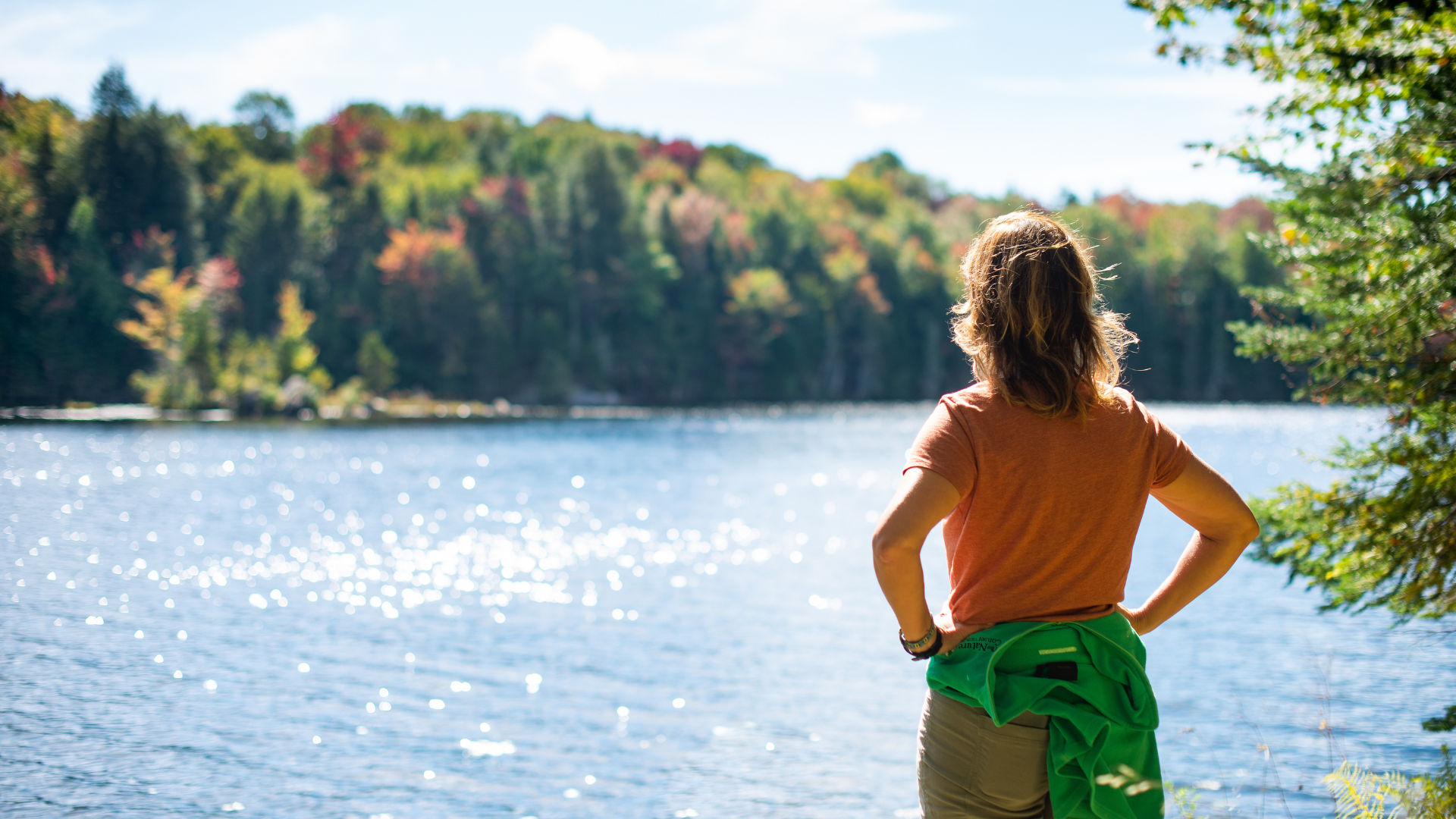 Woman looking into a lake with foliage in the background.