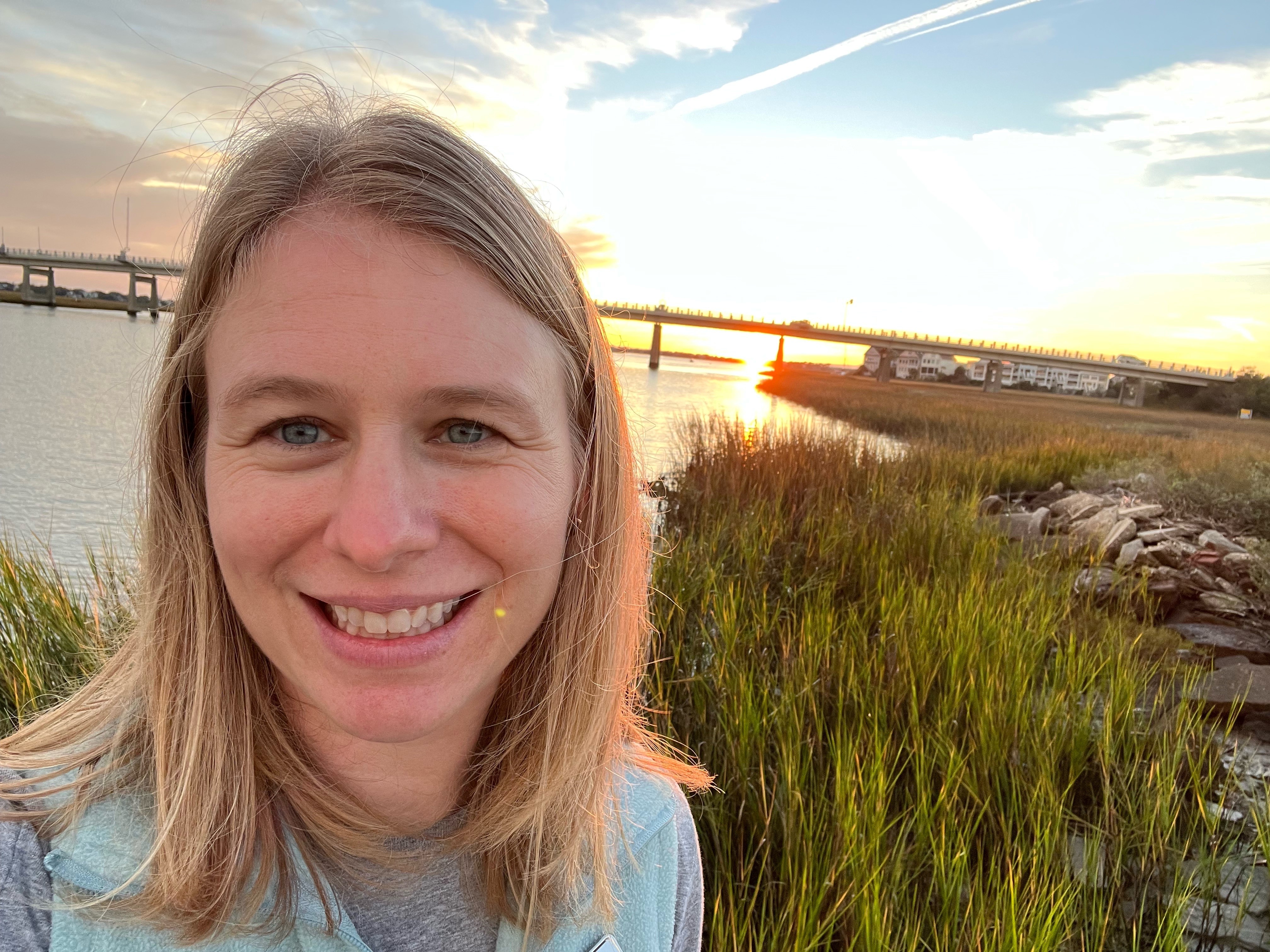 A smiling woman stands in front of a marshland.