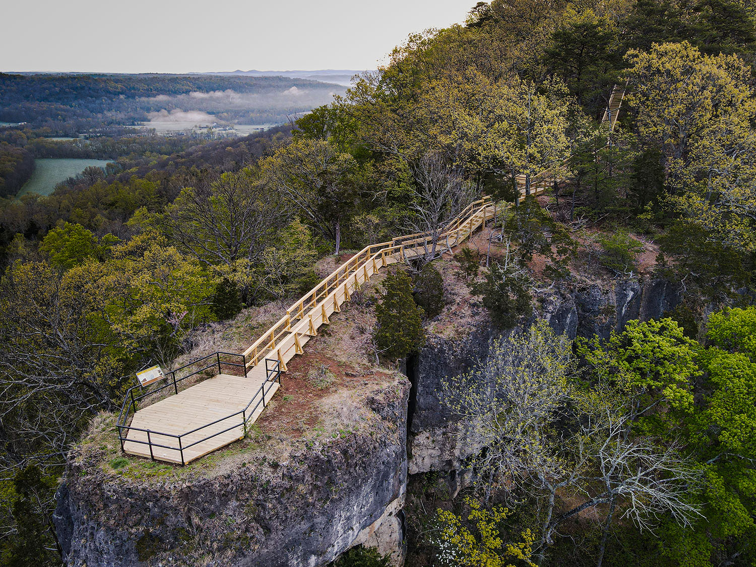 An aerial view of a wooden viewing deck on a forested rocky outcrop.