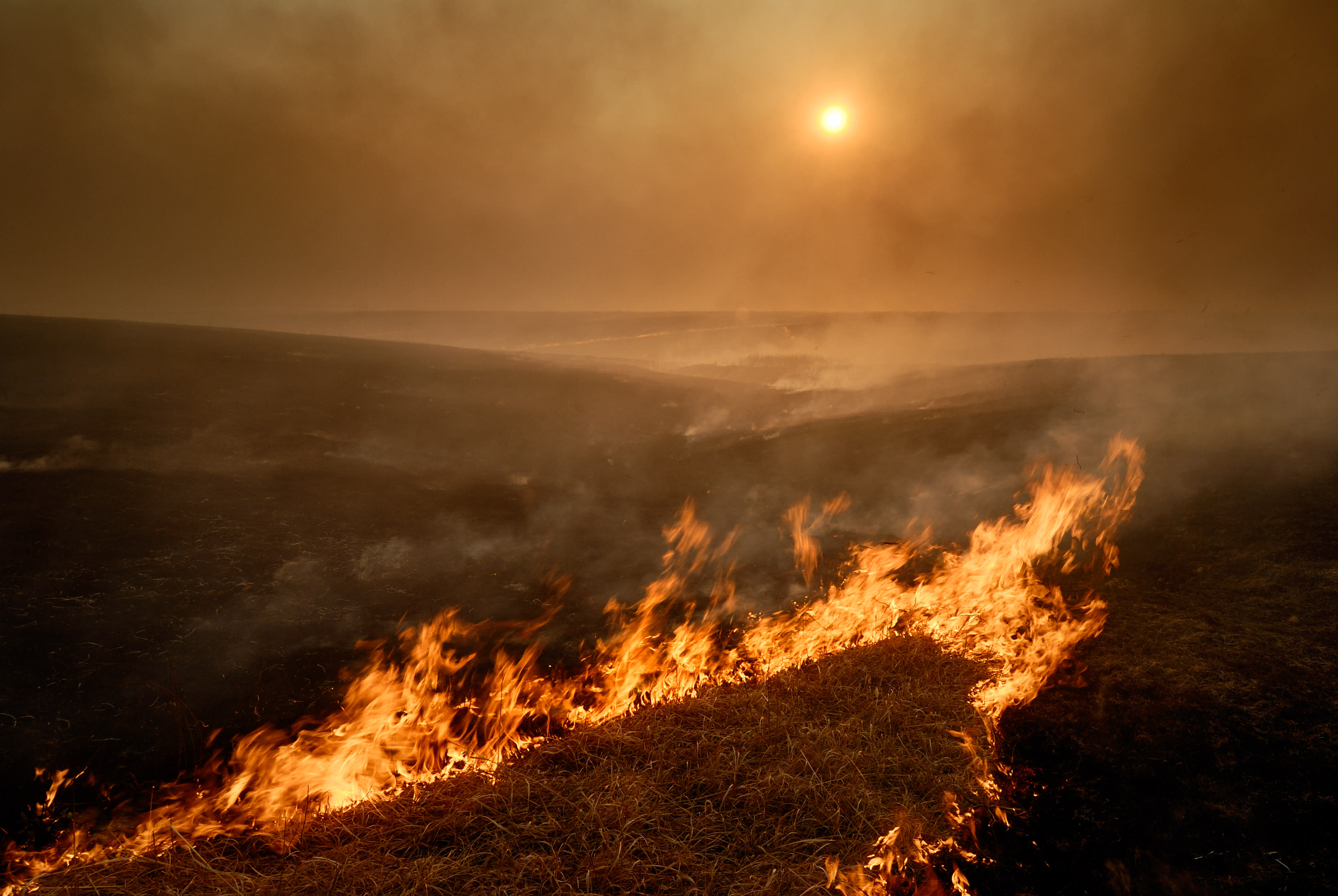 Fire moves across rolling hills, sending smoke into the air.