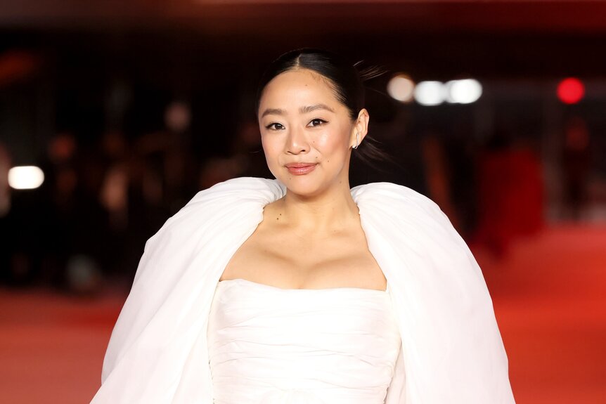 Stephanie Hsu on a red carpet wearing white clothing.