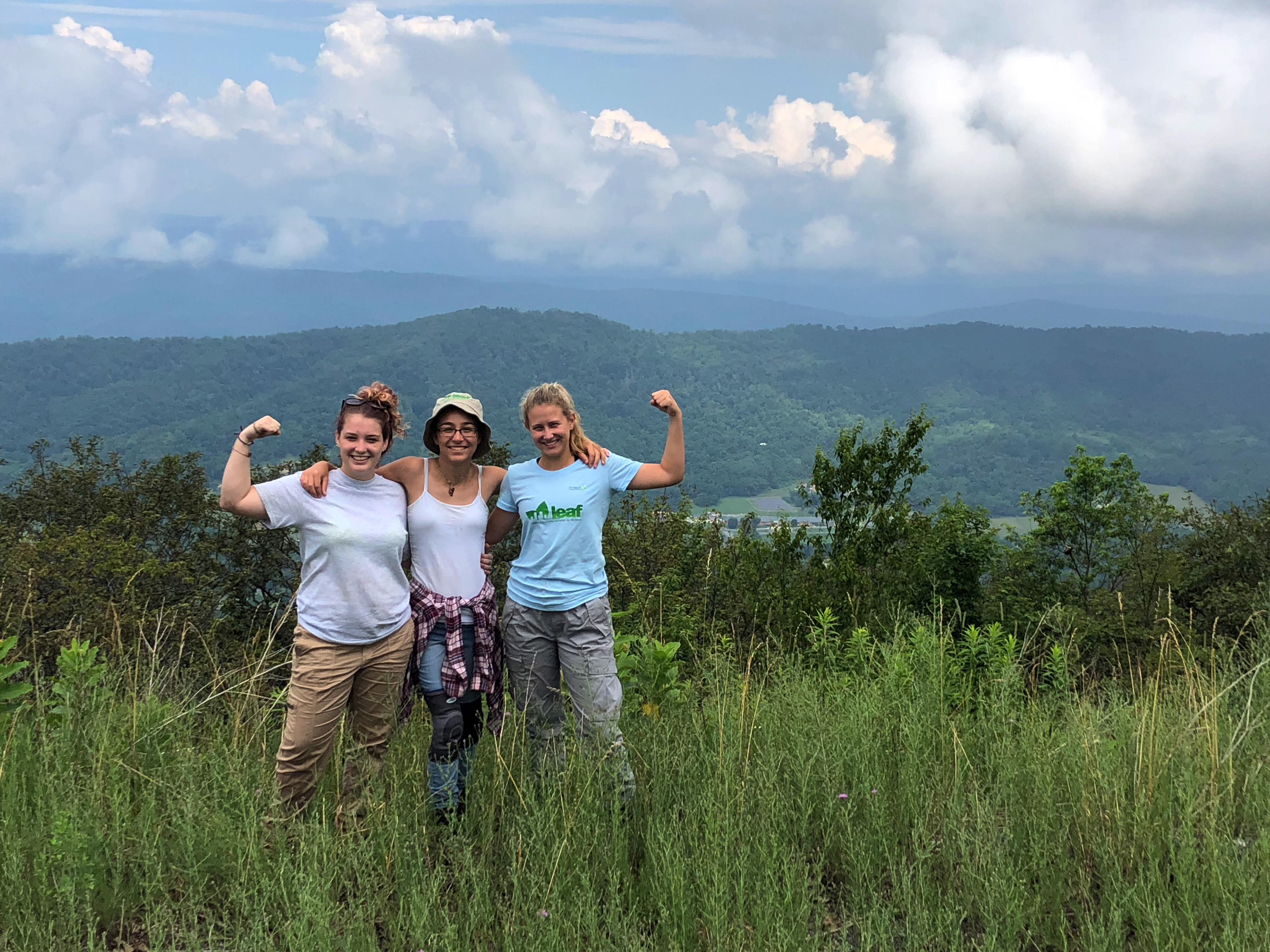 Three women pose arm-in-arm at a mountain overlook.