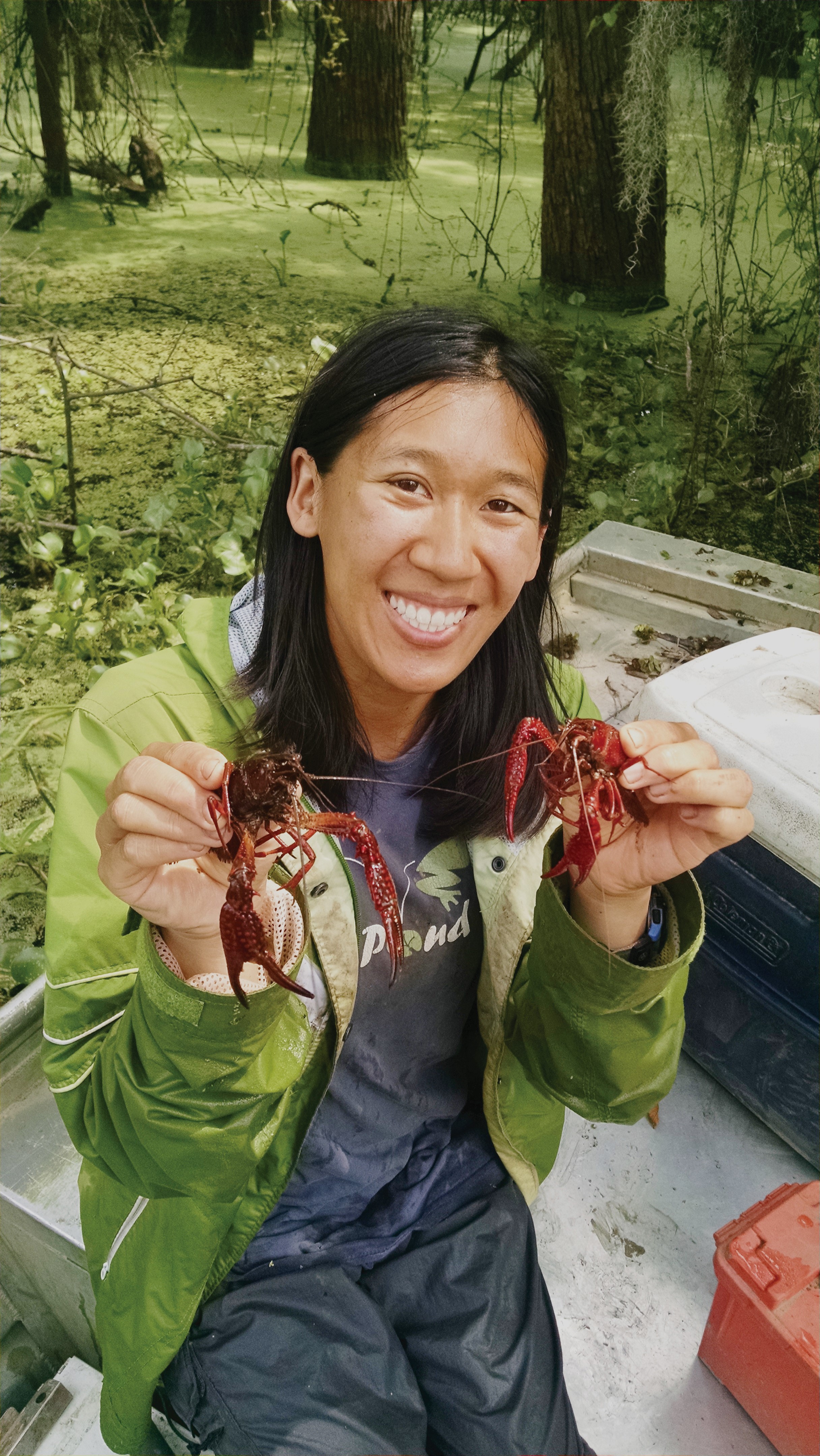 A smiling woman holds up a crawfish in each hand.