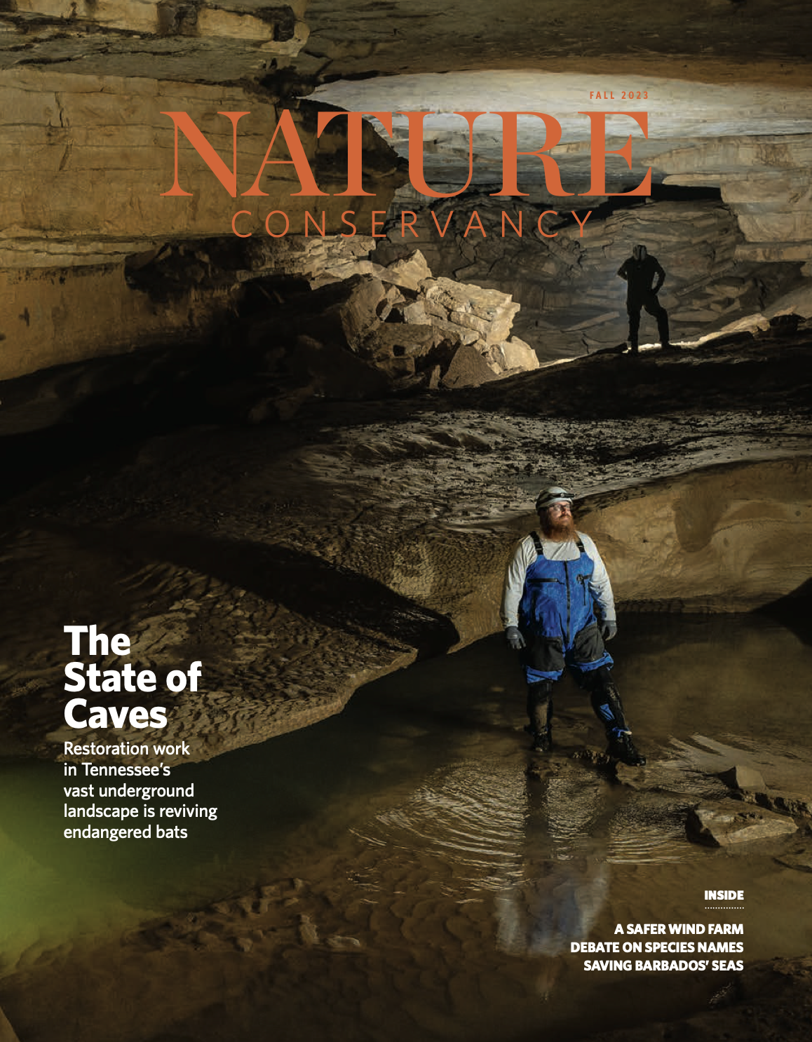 A man wearing a helmet and overalls stands in a cave.