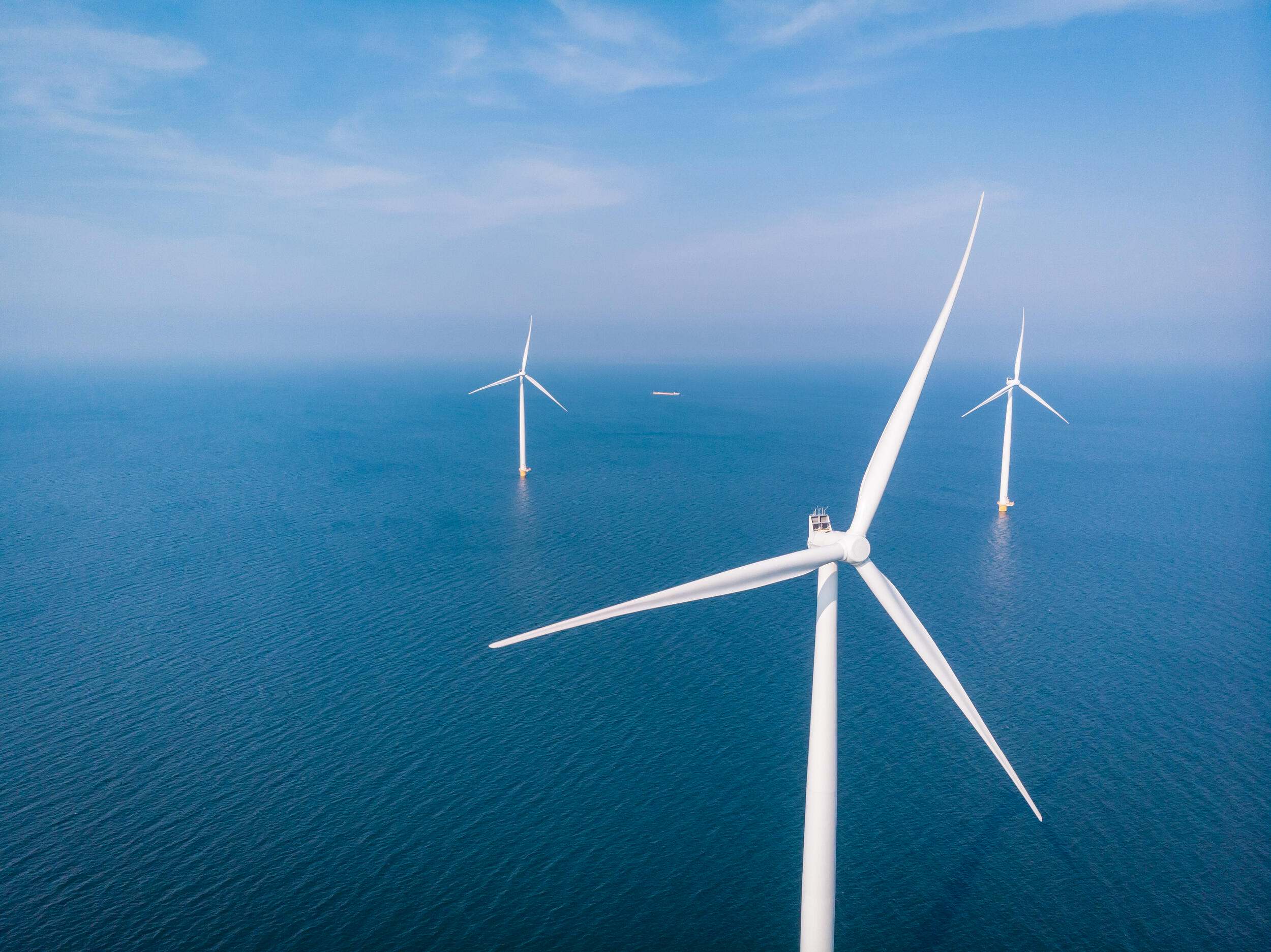 Water surrounds three large white wind turbines.