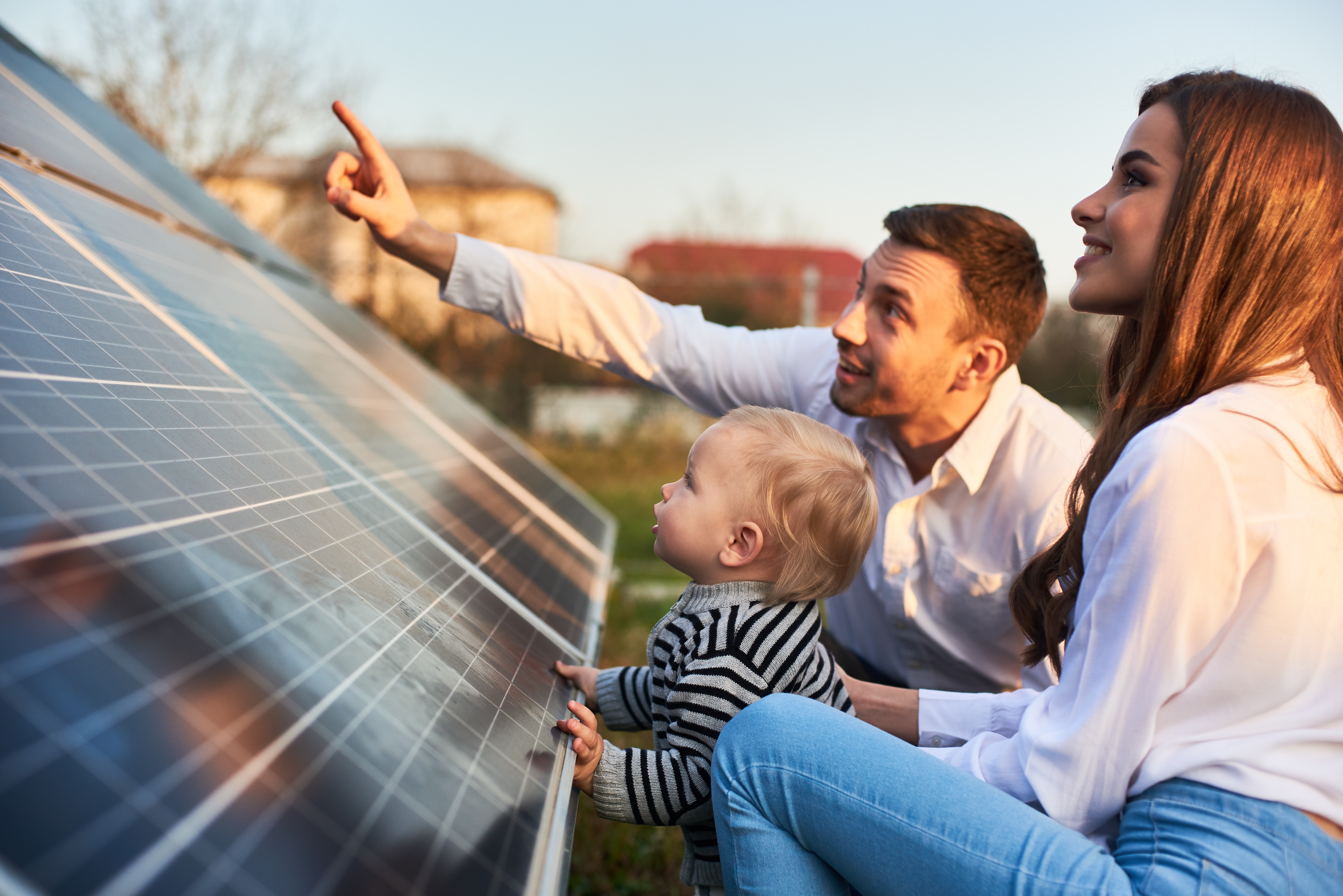 Young woman with a kid and a man in the sun rays look at solar panels. 