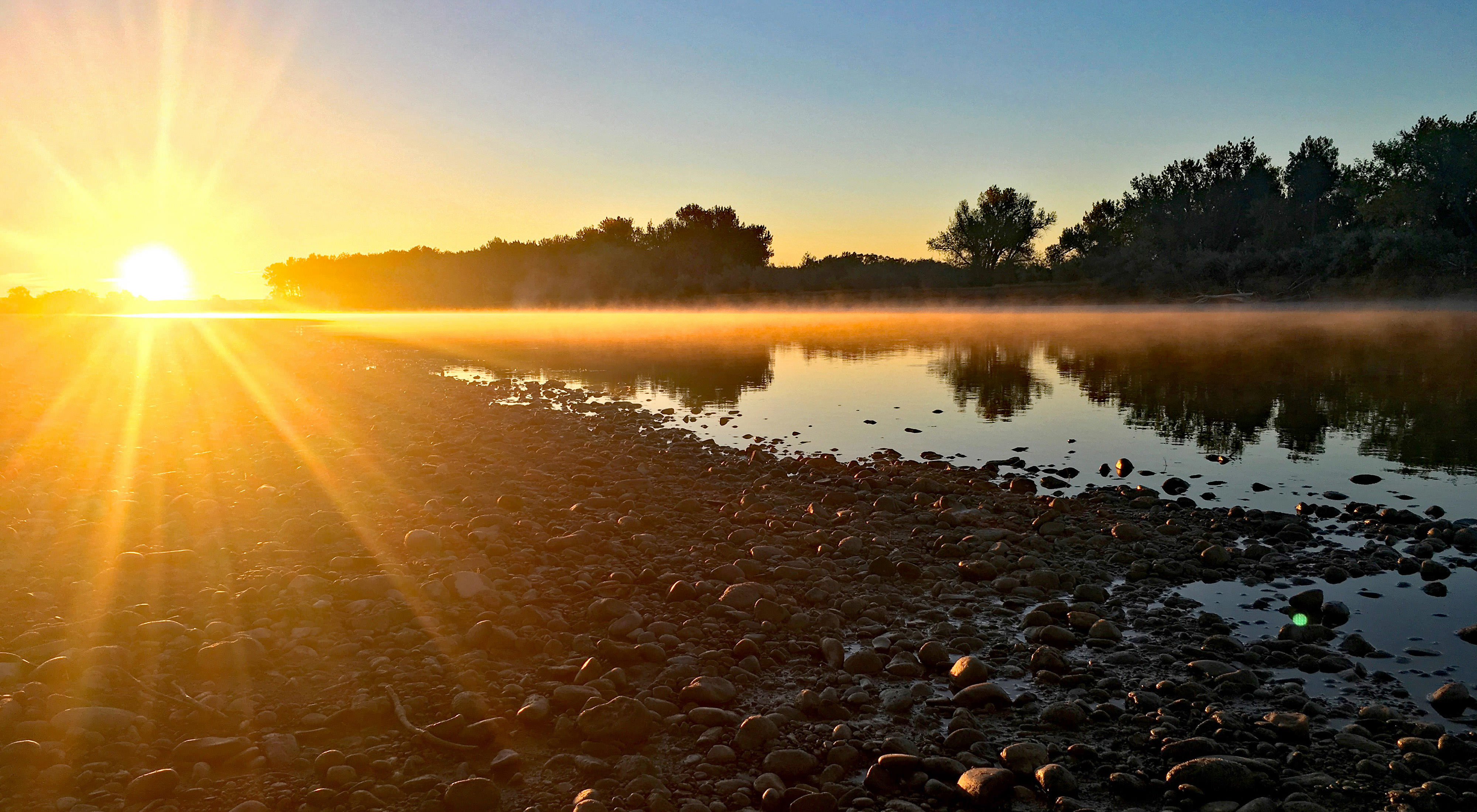 Photo of a sunrise over a river, with rocks in the foreground.