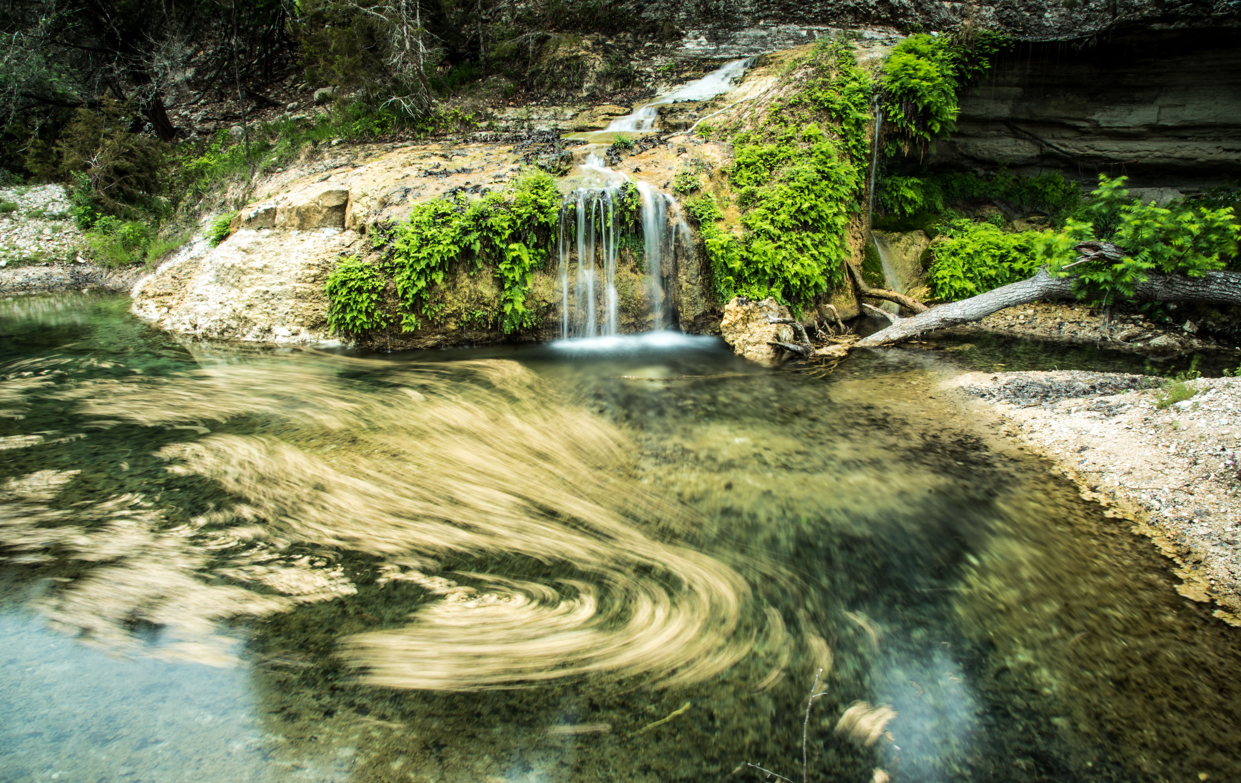 Water falls over limestone covered with moss to feed a small pond with clear water.