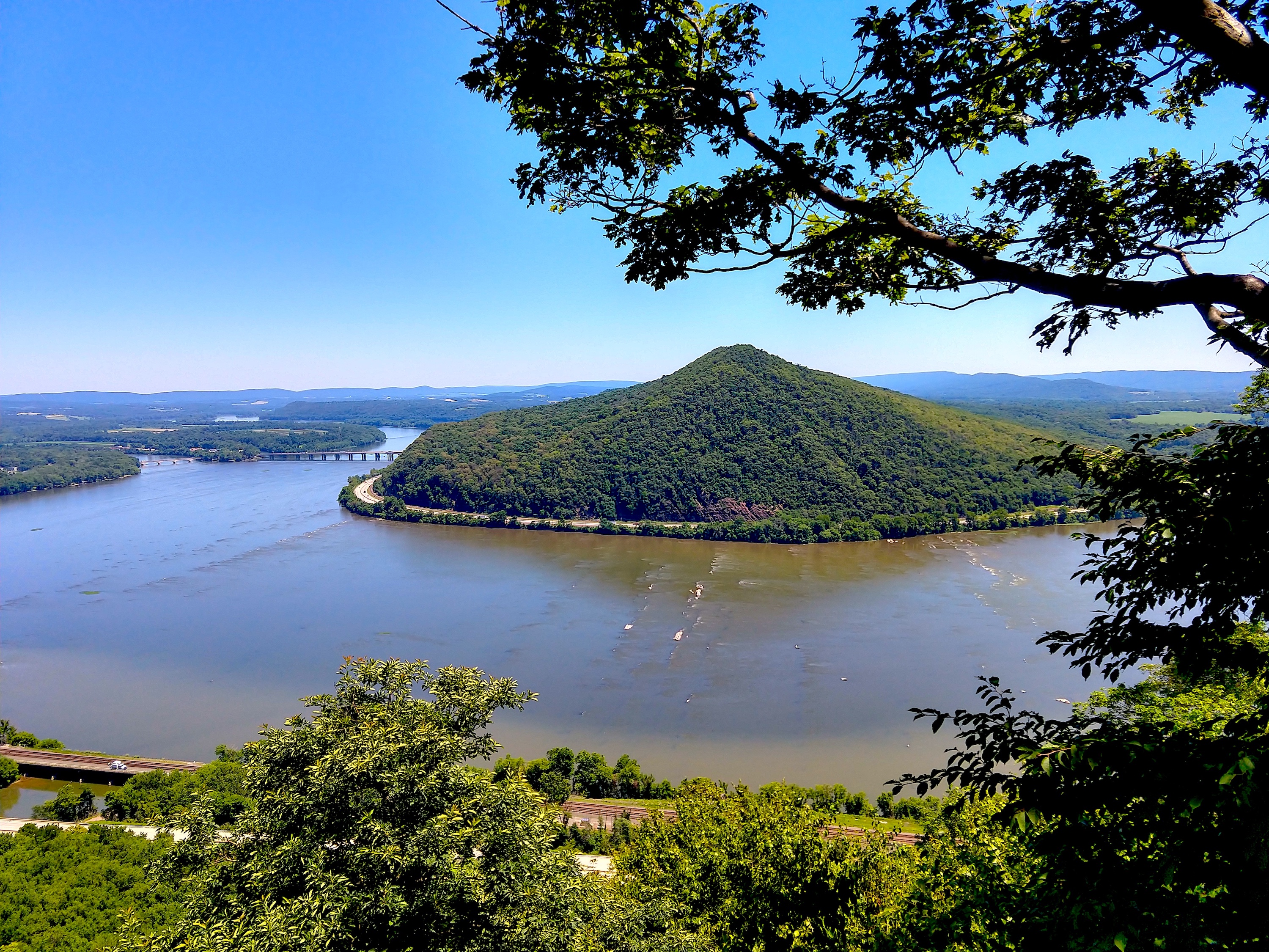 A rock sticks out of the water in front of a small mountain.